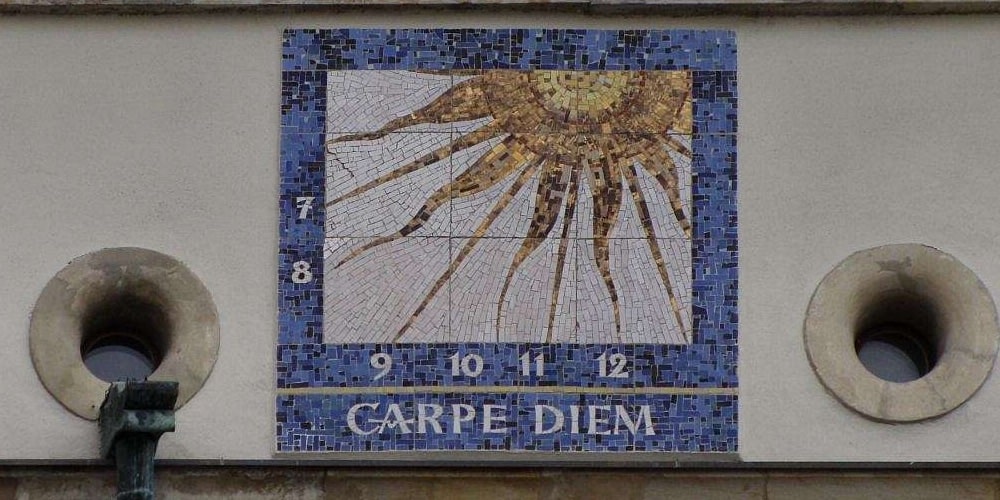 La frase carpe diem escrita en una fachada junto a un reloj de sol.