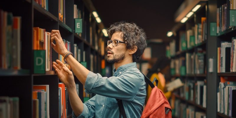 Un hombre busca un libro en una biblioteca.
