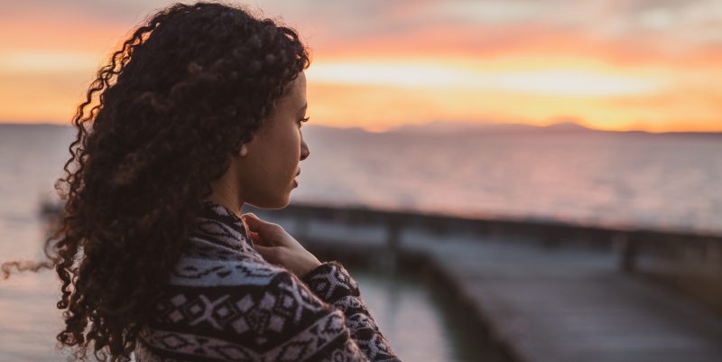Mujer mirando un paisaje al atardecer.
